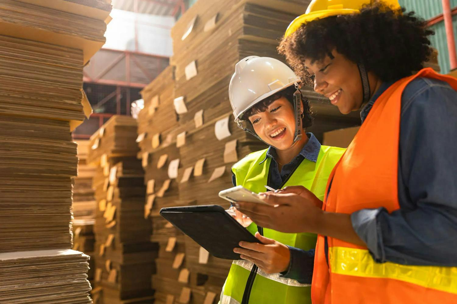 Two female warehouse workers reviewing ipad and phone information (1)