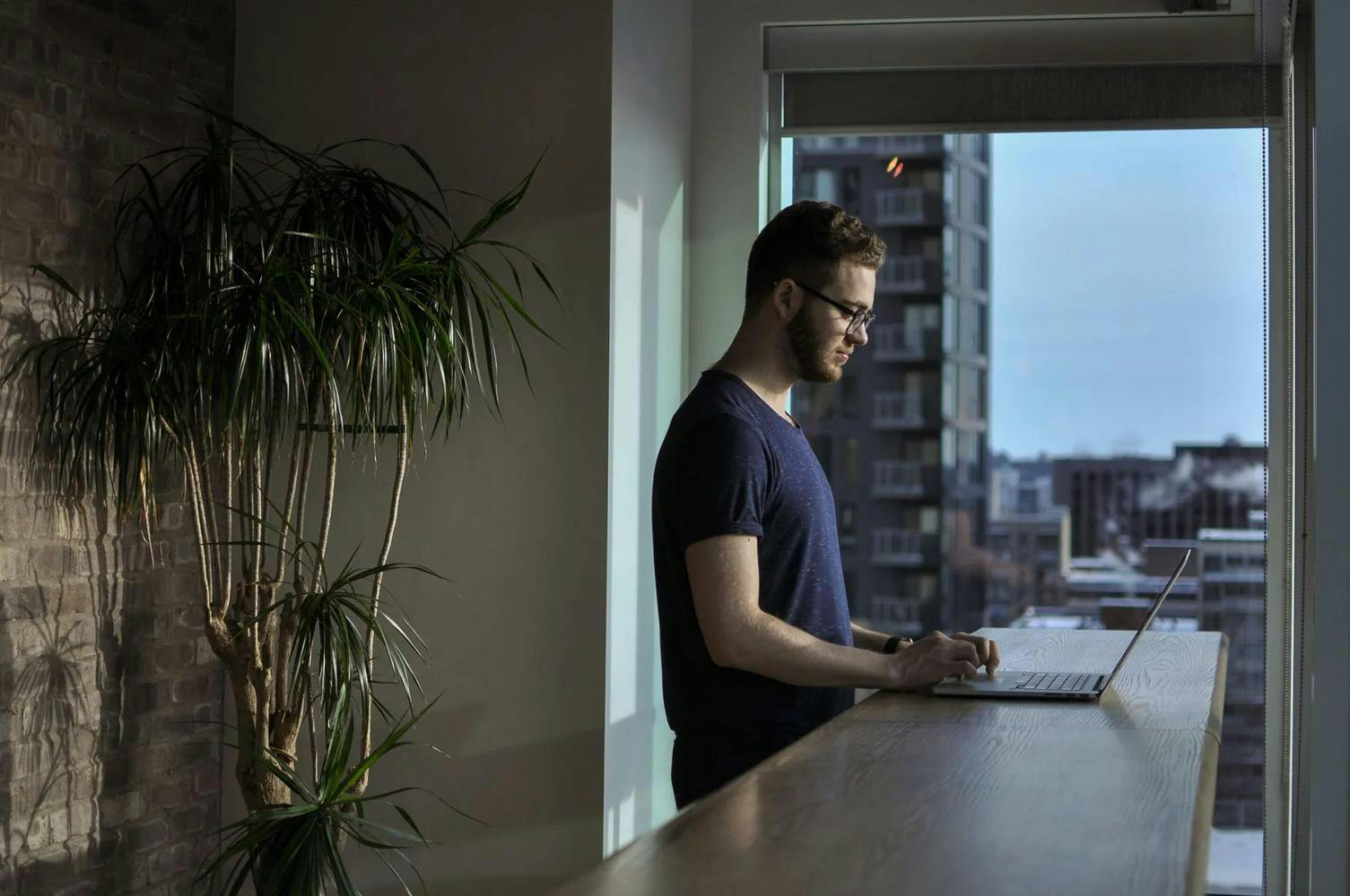 Man standing at laptop on bench in apartment